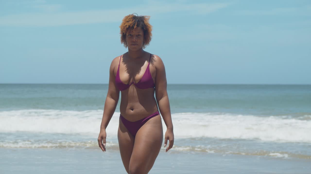Caribbean girl in a sexy bikini walking away from the crashing waves of the ocean on the tropical island of Trinidad