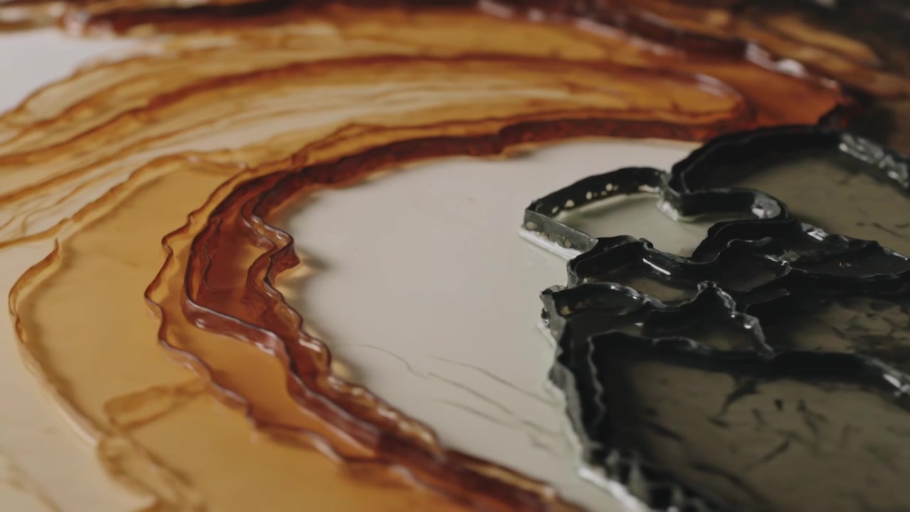 Panning camera revealing fluid art on studio table, showing glossy amber rings and metal gray pools