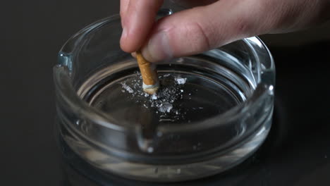 hand putting out a cigarette in empty ashtray