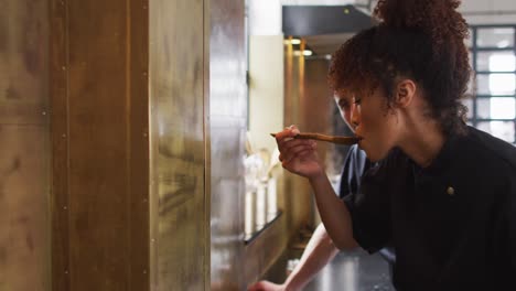 Mixed-race-female-chef-preparing-a-dish-and-smiling-in-a-kitchen-