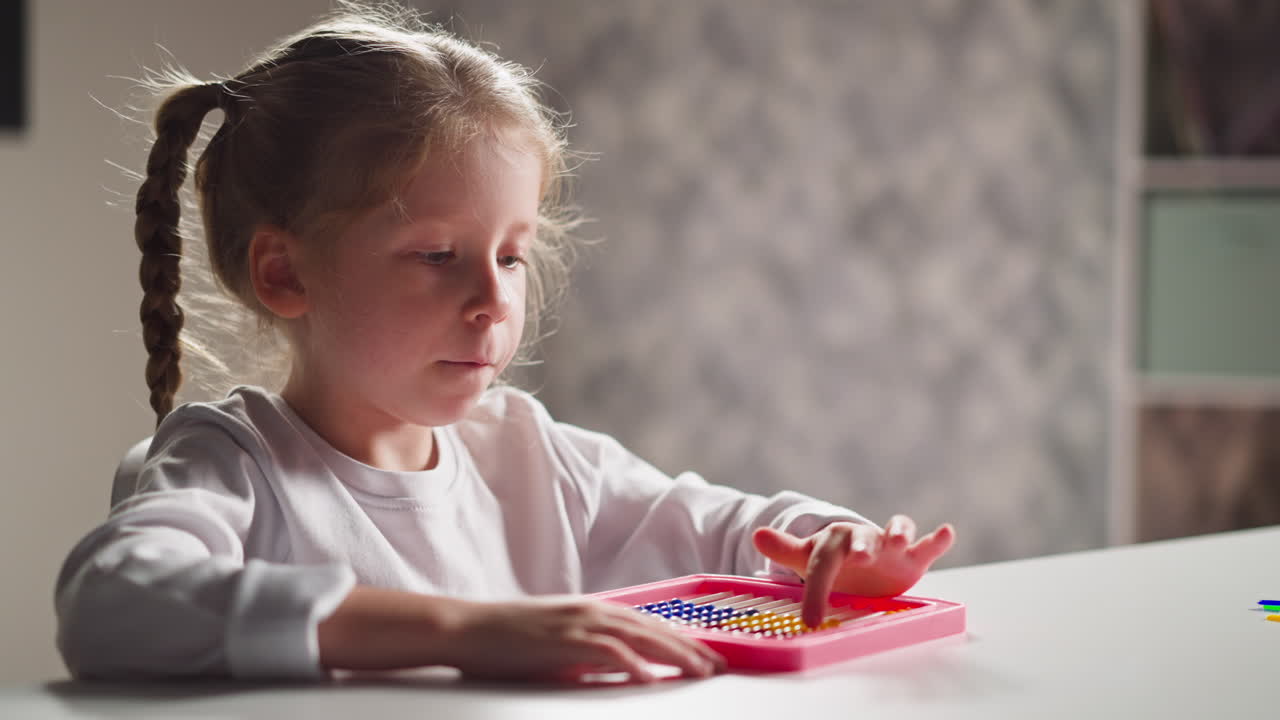 Una piccola bambina ispirata impara a contare con un abaco giocattolo alla scrivania.
