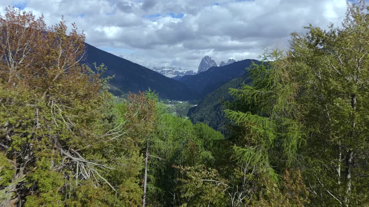 fotografía aérea que captura los valles boscosos y los lejanos picos de las montañas de val gardena en las dolomitas, italia, con pueblos dispersos y exuberante vegetación