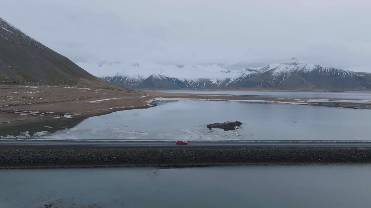 아이슬란드의 멋진 풍경에서 빙하 호수를 나누는 도로에서 움직이는 빨간 차의 추적 드론  ⁇