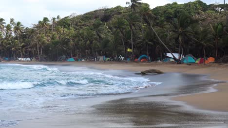 Tribal-Gathering-festival-at-Playa-Chiquita-Beach-in-Panama-with-tents-near-the-shore,-Handheld-wide-shot