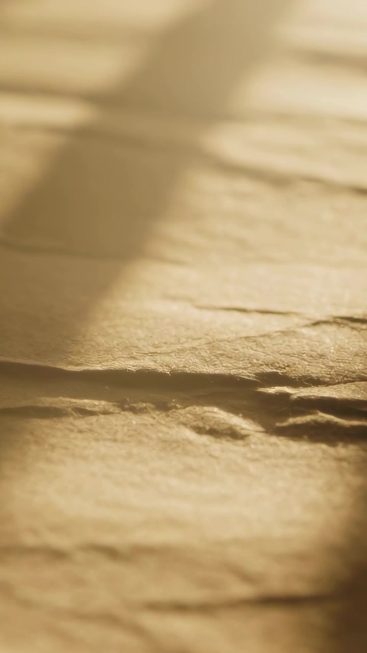 Vertical video: Blinds shifting, shadow moving across kraft paper on desk, showing creases, fibers