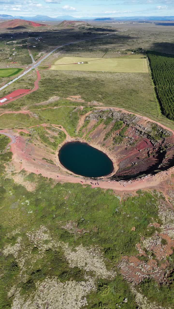 Wide rotating drone view around the Kerid crater volcanic lake in Iceland, vertical video.