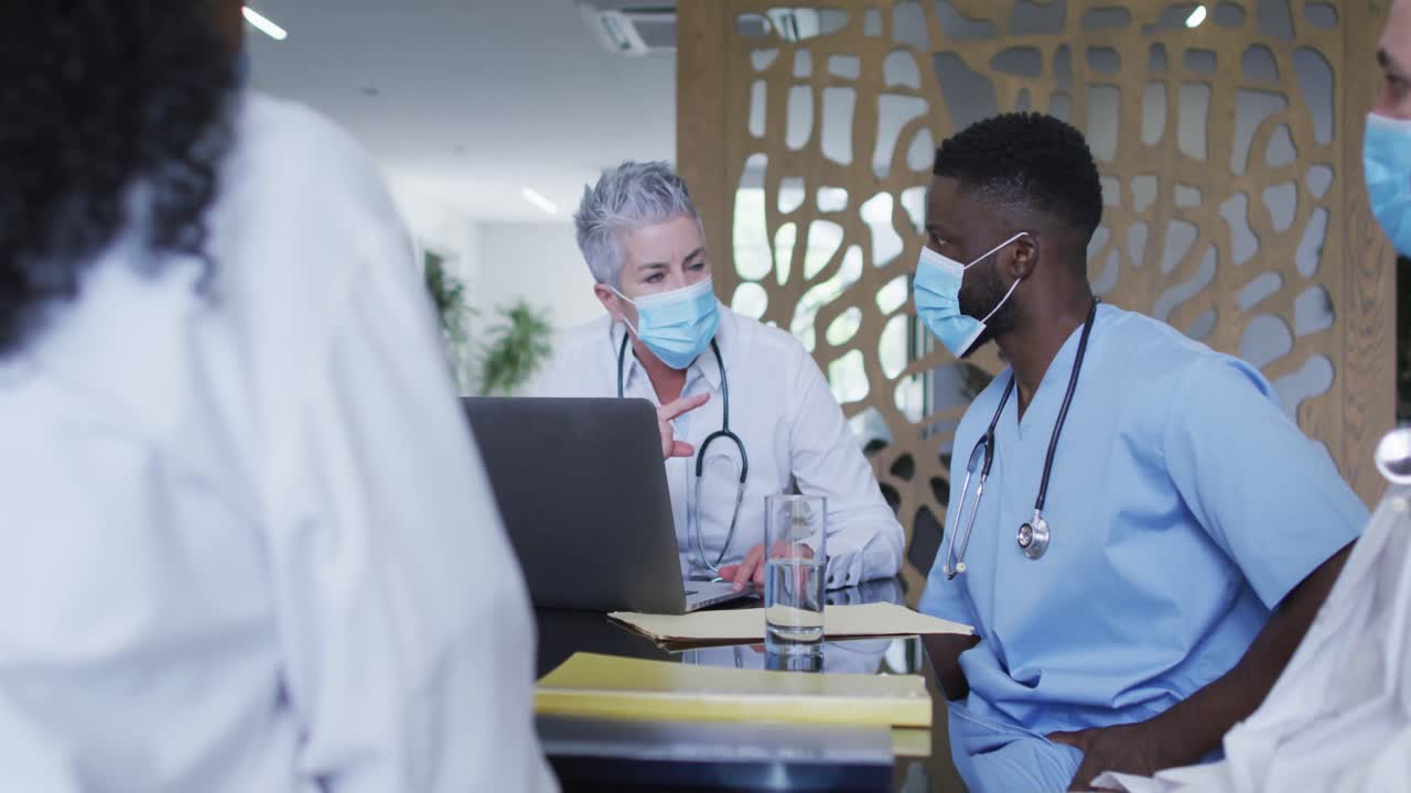 Caucasian female senior doctor and diverse hospital colleagues wearing face masks talking at meeting