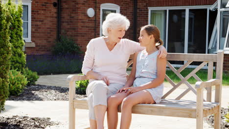 Granddaughter-Sitting-On-Bench-With-Grandmother-During-Visit-To-Retirement-Home