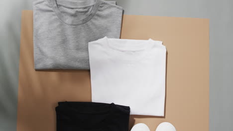 video of flat lay of multi coloured t shirts with copy space on brown and grey background