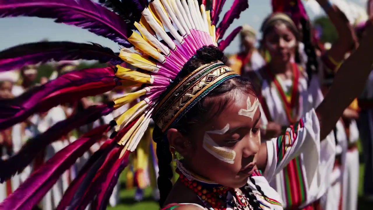 Junges indigenes Mädchen mit farbenprächtigem Federkopfschmuck tanzt traditionellen Tanz