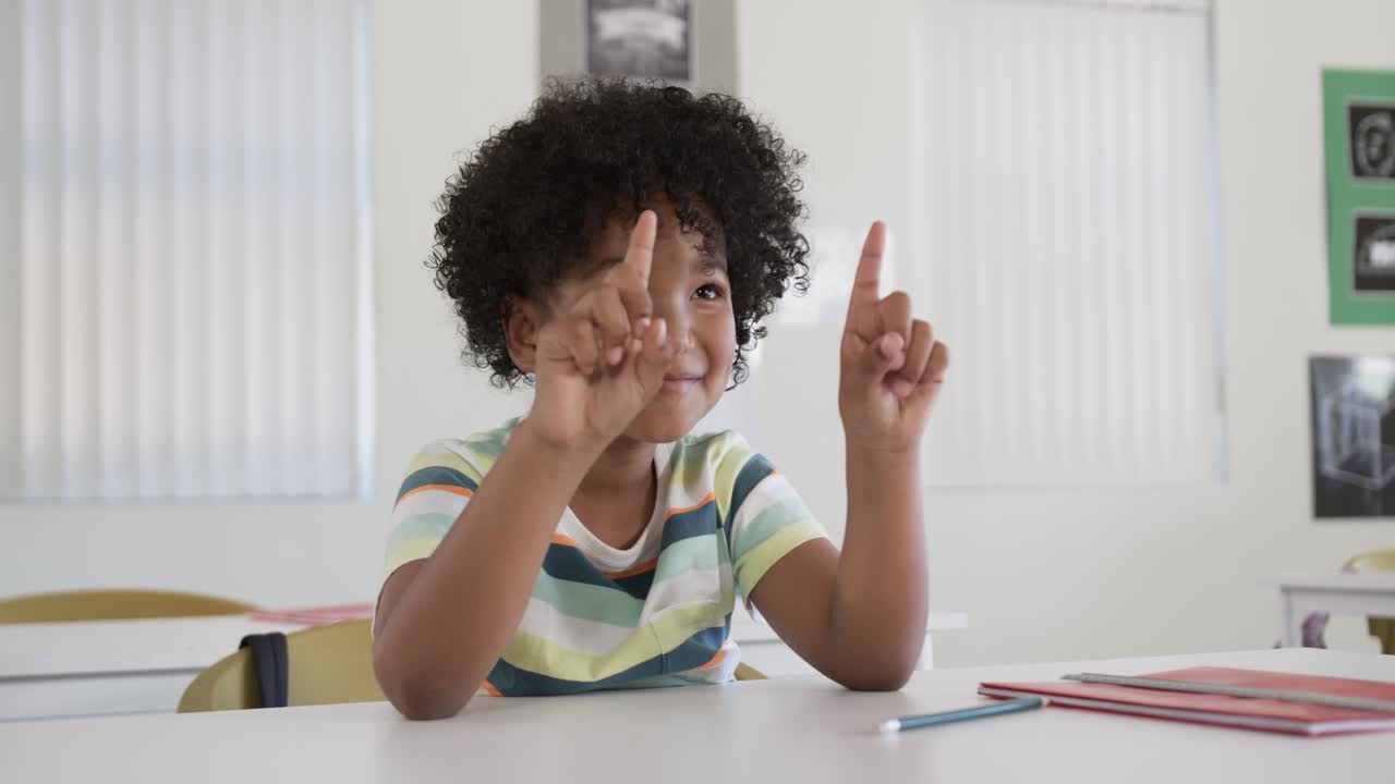 Bambino africano che guarda fuori campo alzando gli indici puntati e abbassando le mani in classe con una matita