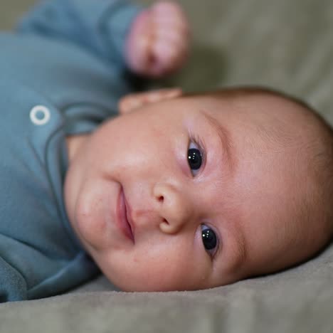toddler in a blue suit waving with his hands. little kid facing camera lying on the bed. close up