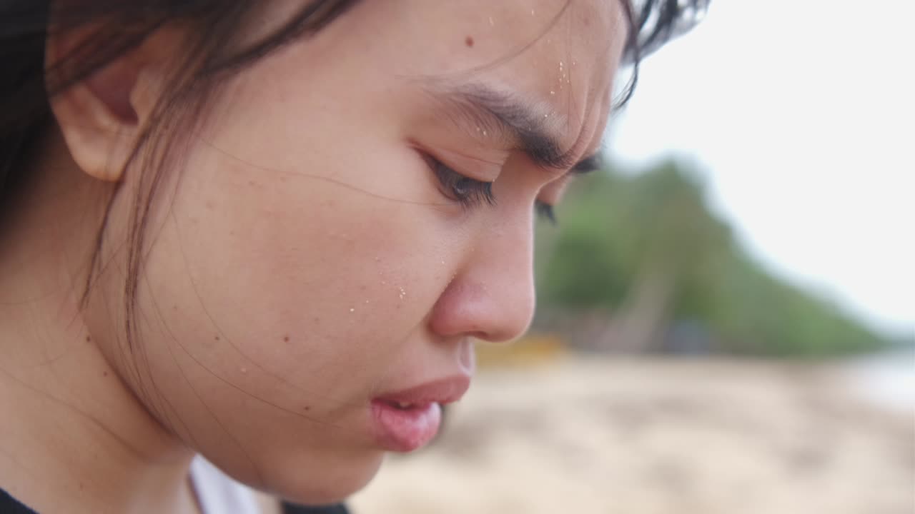 Close-up of young woman's face as she experiences anxiety attack while crying at windy, outdoor setting. -static shot