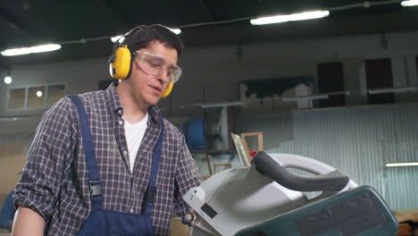 hombre con gafas protectoras y auriculares cortando tablones de madera con sierra circular eléctrica