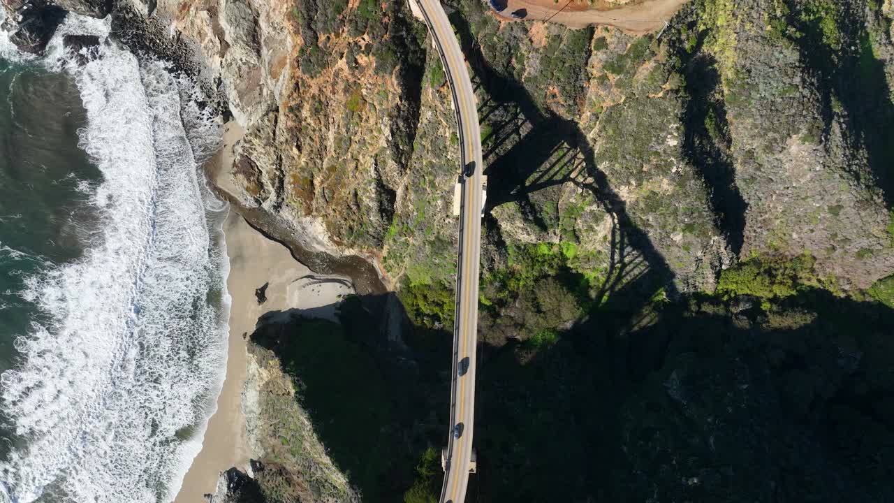 bixby bridge highway 1의 조감도, 파도가 해안에 충돌할 때, 녹색 언덕을 따라 다리의 아치형 그림자, 캘리포니아