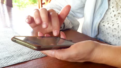 cerca de las manos de las mujeres enviando mensajes de texto, mensajería, comunicación y socialización con amigos en teléfonos móviles android en una mesa de madera en un restaurante de cafetería