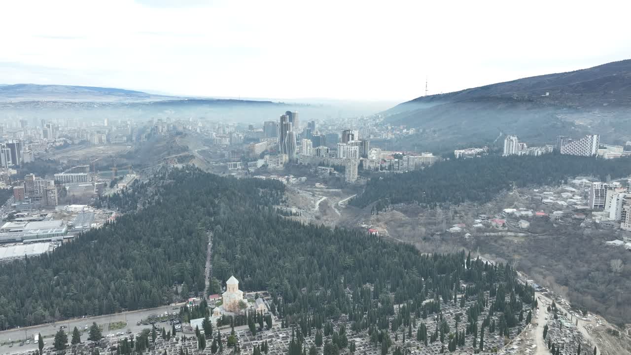 an aerial view of a city blending green parks, dense urban areas, and rolling hills. The urban sprawl contrasts with the natural beauty of surrounding vegetation and open spaces