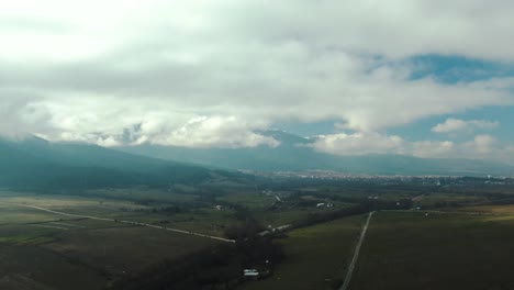 Toma-De-Un-Dron-De-Una-Montaña-De-Campo-Y-Una-Ciudad-En-El-Fondo-Con-Cielo-Nublado