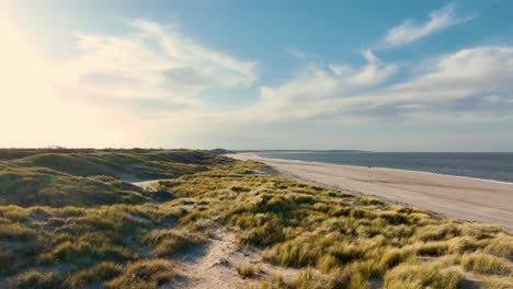 long aerial shot flying over grassy dunes along an empty beach during a beautiful sunset