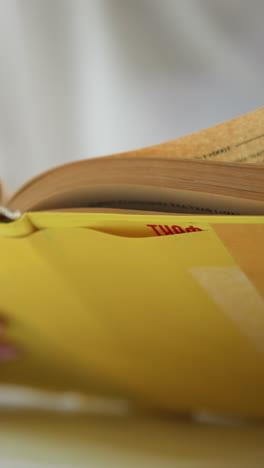 primer plano de un libro amarillo abierto con fondo de enfoque suave y manos sosteniendo páginas, haciendo hincapié en la lectura y el aprendizaje en un entorno tranquilo y sereno