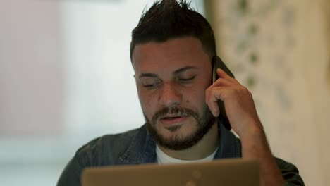 hombre serio hablando por teléfono inteligente y usando computadora portátil en un café