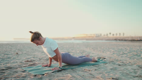 full length shot of caucasian woman exercising yoga on mat by the sea.