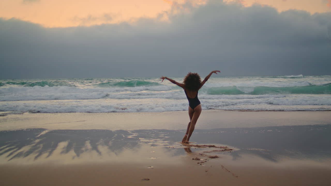 niña bailando arena húmeda cerca de las olas del océano noche nublada. mujer bailando.
