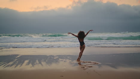 girl dancing wet sand near ocean waves cloudy evening. woman performing dance.