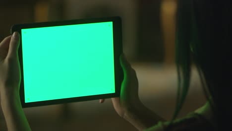 black hair teen girl is holding tablet with green screen in landscape mode at evening time. casual lifestyle.