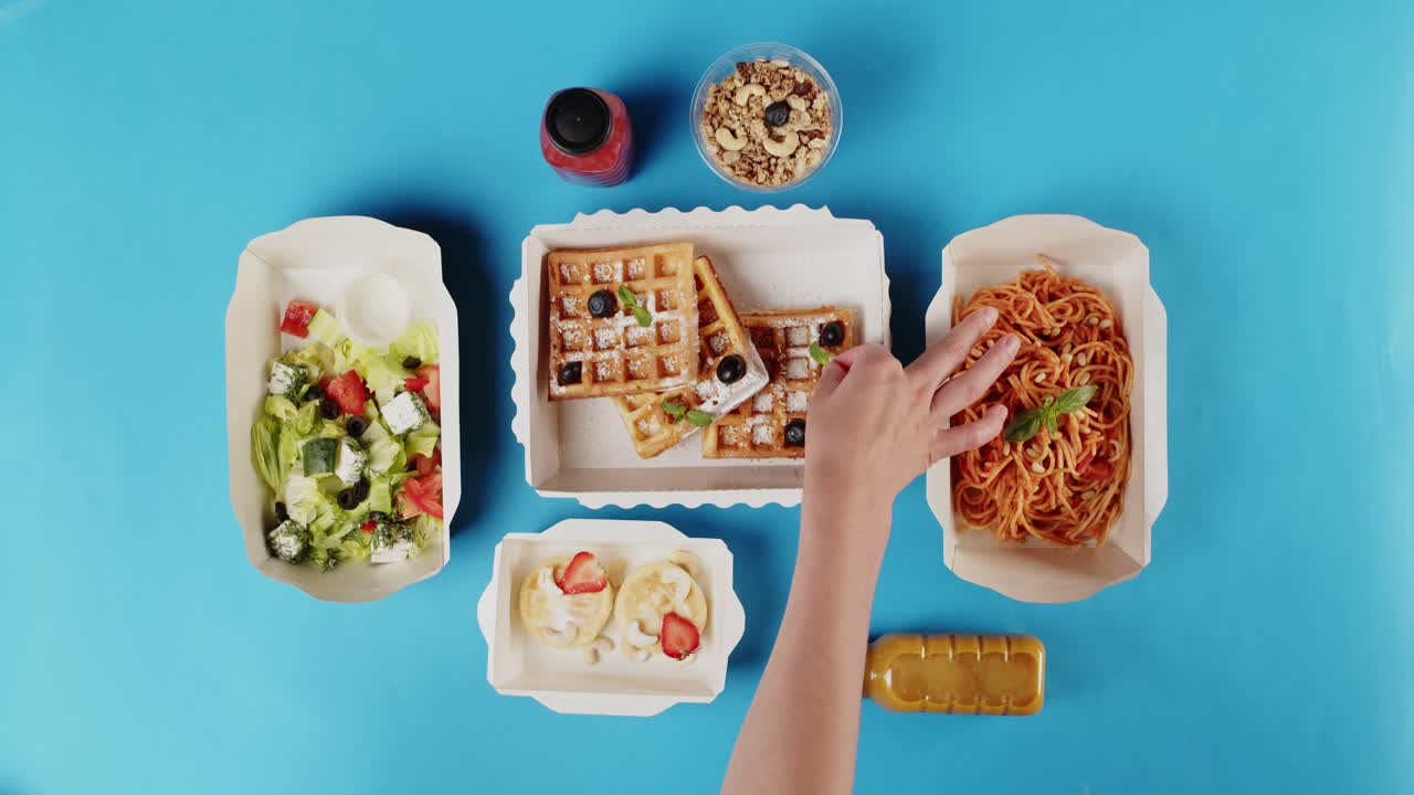 Mano disponiendo comida saludable para llevar sobre fondo azul