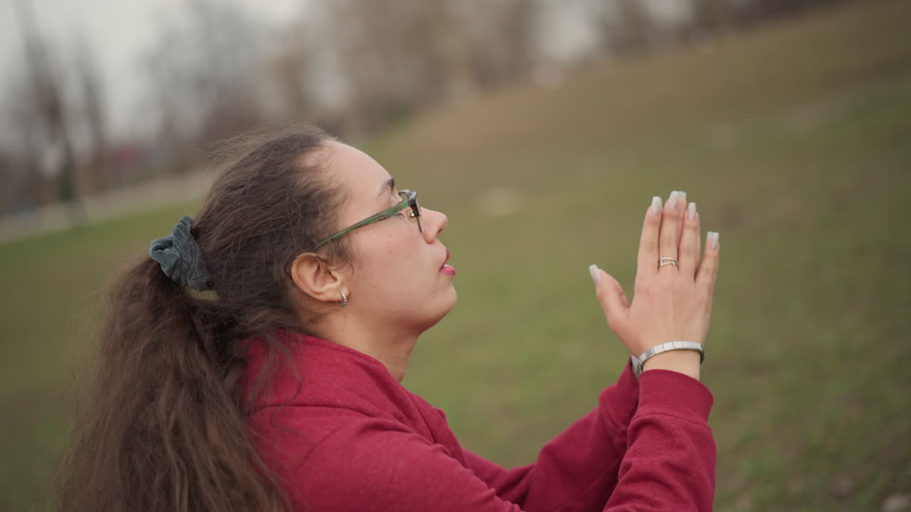 Focused Woman Stretching Outdoors, Asian Woman Engaged In Mindful Stretching Under Cloudy Sky, Tranquil Female Performing Controlled Breathing And Gentle Stretches Amidst City Greenery