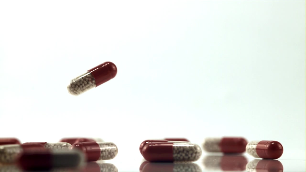 Capsule mediche rosse e trasparenti che cadono al rallentatore su sfondo bianco