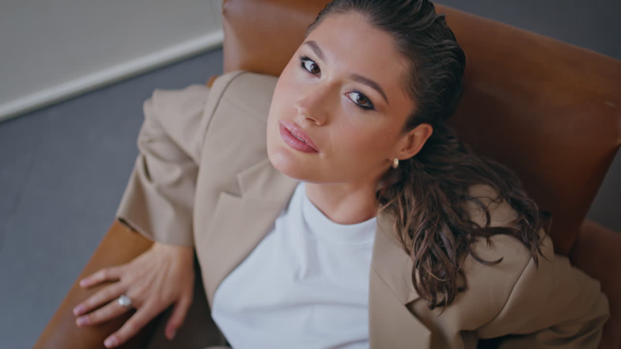 mujer confiada descansando en el sillón mirando cámara de primer plano vista superior. modelo posando