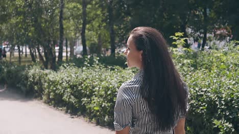 backside view long haired brunette girl walks in green park