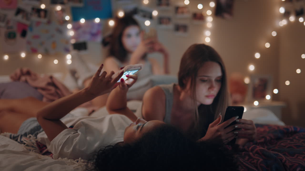 adolescentes felices acostadas en la cama usando teléfonos inteligentes navegando por las redes sociales enviando mensajes de texto disfrutando de dormir el fin de semana