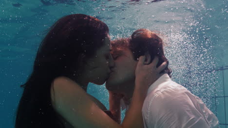 Pareja-Romántica-Besándose-Bajo-El-Agua-En-La-Piscina-Vistiendo-Ropa-Jóvenes-Enamorados-Disfrutando-De-Besos-íntimos-Amantes-Sumergidos-En-Agua-Flotando-Con-Burbujas-En-Intimidad-Apasionada