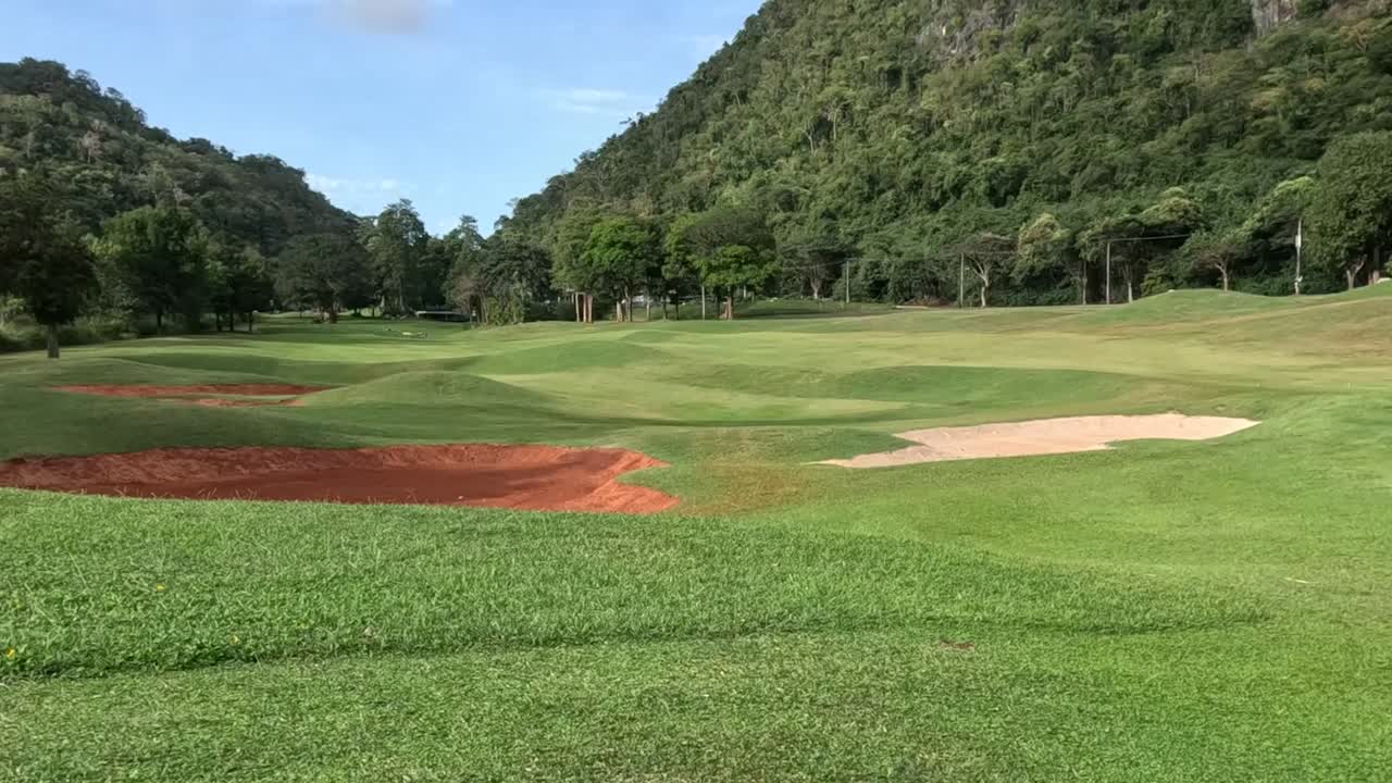 A serene golf course nestled against a verdant hillside, featuring sand traps and expansive green fairways.