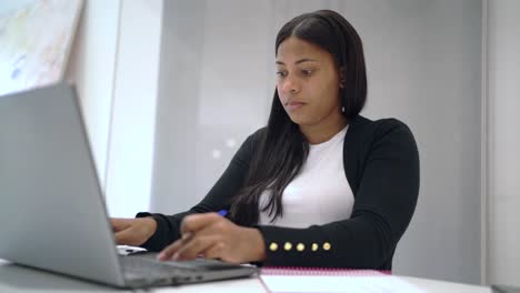 mujer negra seria trabajando en una computadora portátil en la oficina