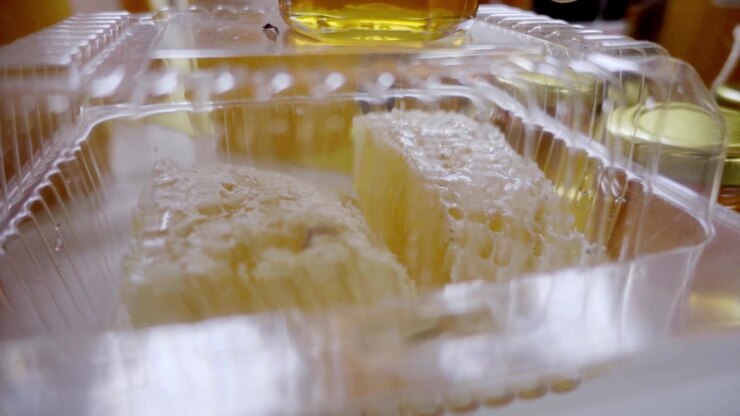 Closeup view of golden honeycomb blocks inside transparent container, rich texture and natural pattern highlighting raw honey product and food freshness