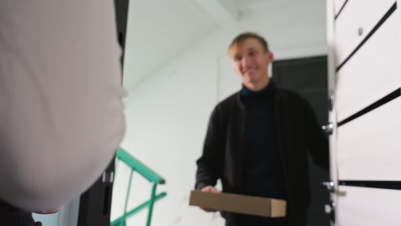 Una cliente riceve un pacco alla porta, un corriere scansiona il pacco mentre la destinataria firma sul telefono all'ingresso dell'appartamento, primo piano delle mani che si scambiano il pacco, luce serale, momento di consegna urbano e amichevole