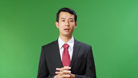 young asian businessman in suit jacket standing and presenting something on green screen background, chroma key