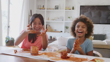 two pre-teen girls using modelling clay laughing and showing their dirty hands to camera, front view