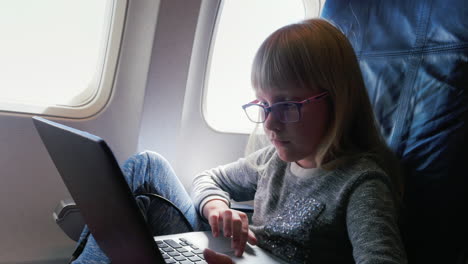 a young business woman in glasses flies in an airplane uses a laptop