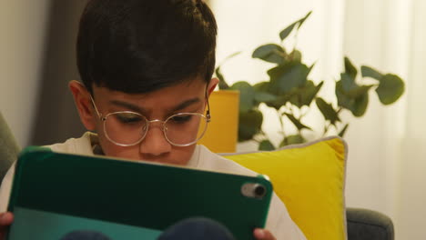 close up of young boy sitting on sofa at home playing games or streaming onto digital tablet 1