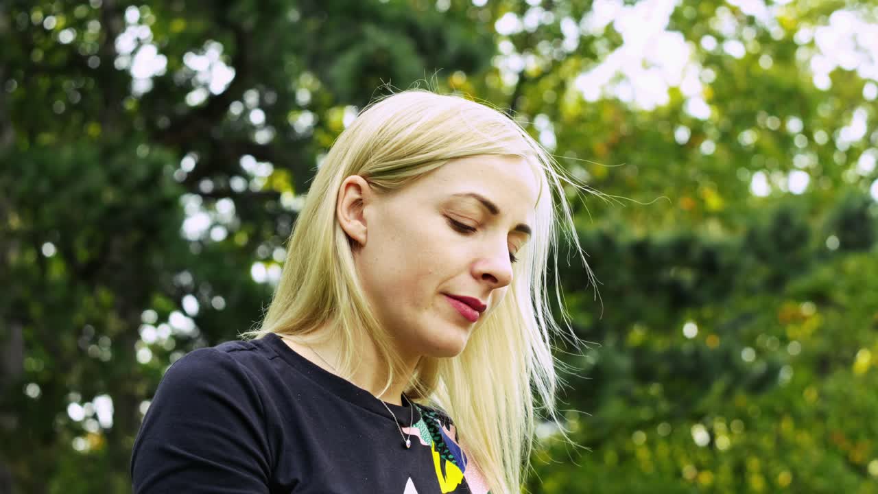 Relaxed blonde woman sits in leafy park and eats chocolate in early autumn light