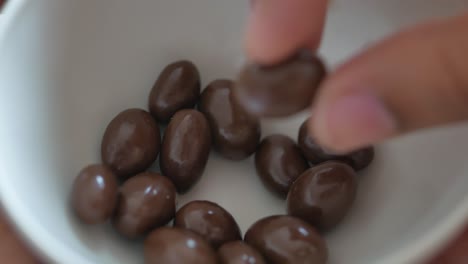 close-up of a hand picking up chocolate candies from a white bowl