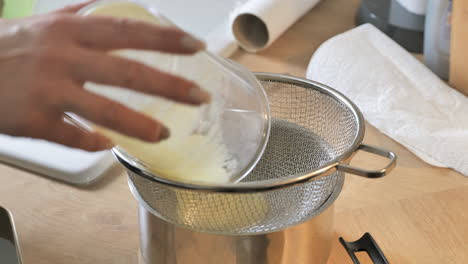 person pouring thick liquid of smoothie into colander in kitchen, close up