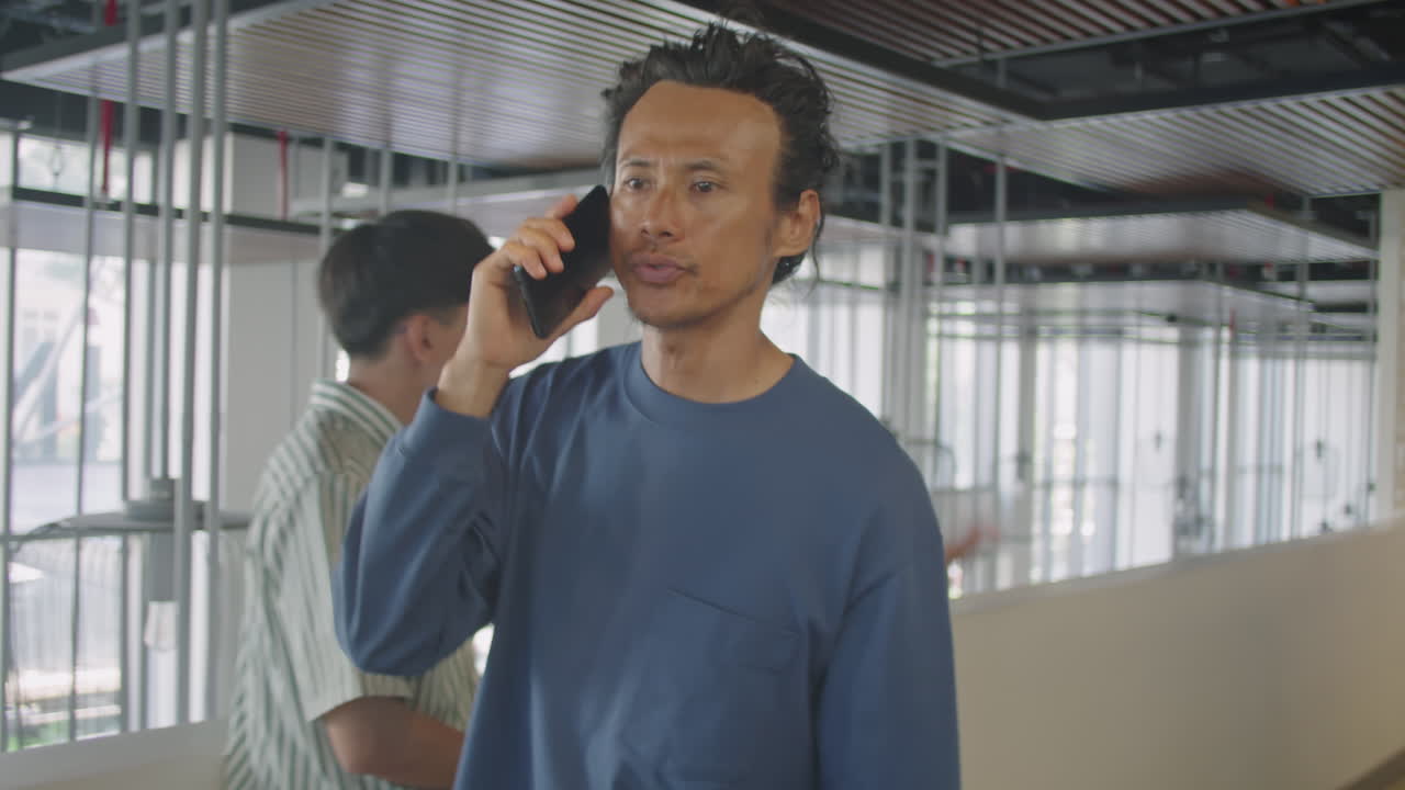 Asian Man Walking in Office and Talking on Phone