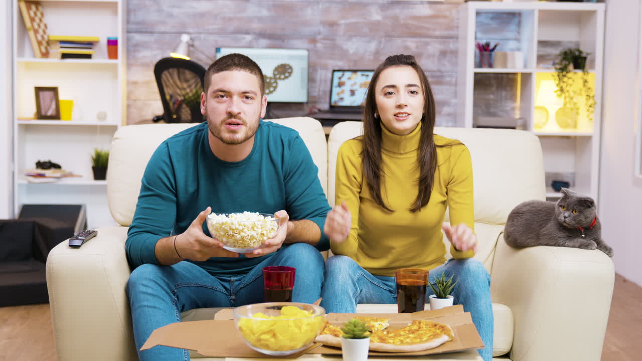 Casal assistindo à TV e comendo lanches