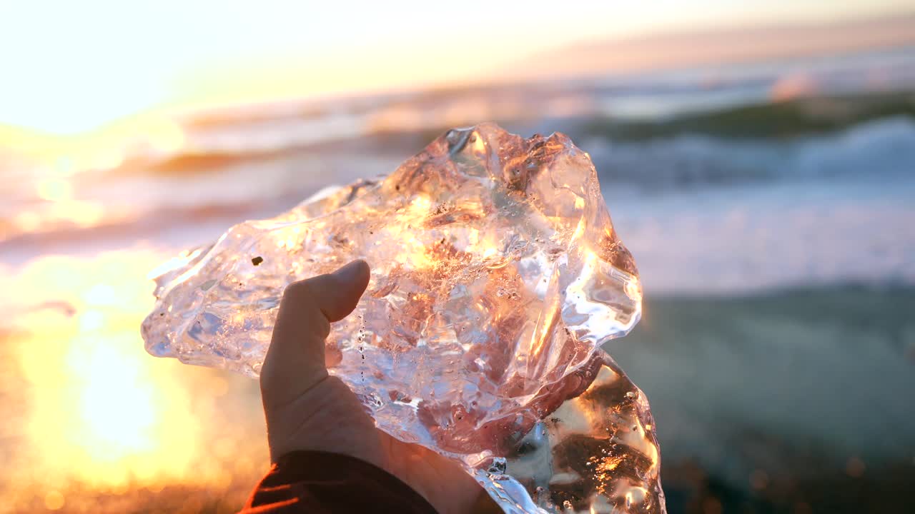 Holding a piece of ice on the beach at sunset
